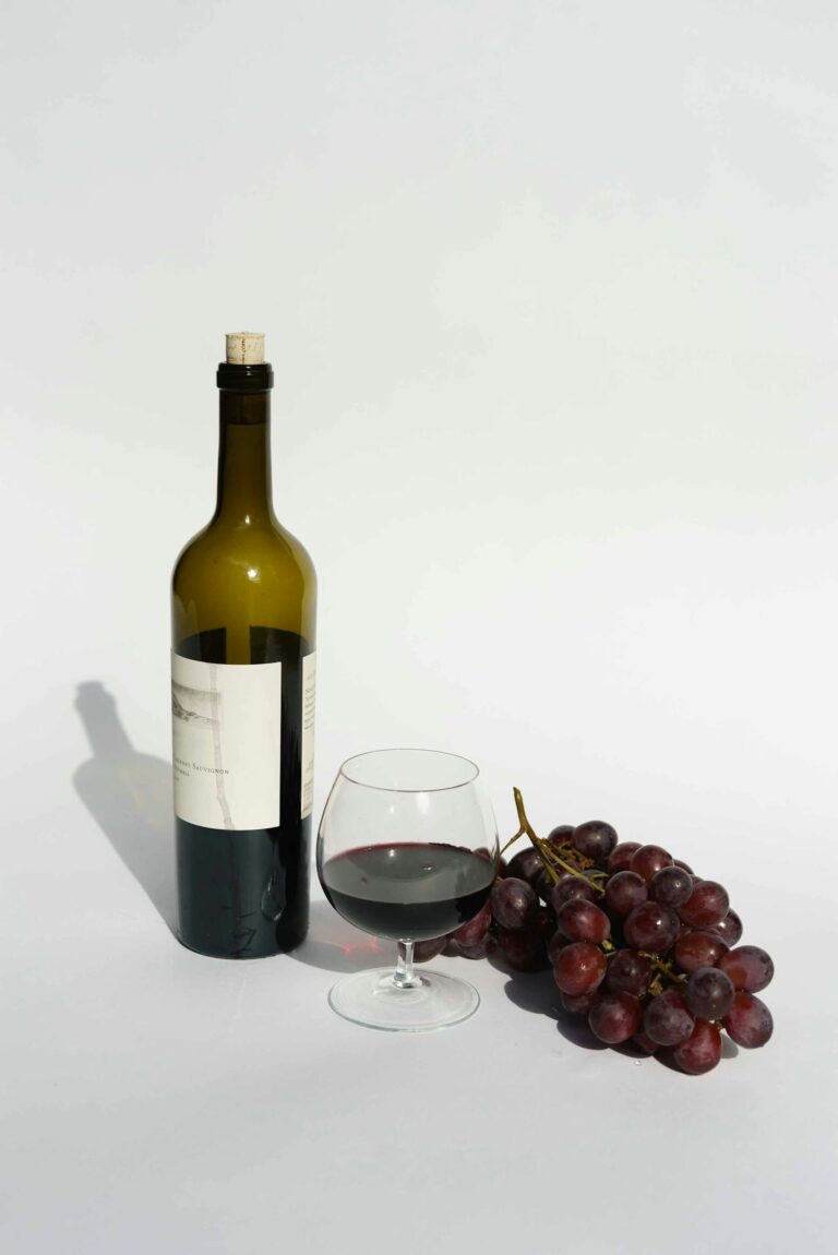 A sophisticated still life featuring red wine, a wine bottle, and fresh grapes on a white background.